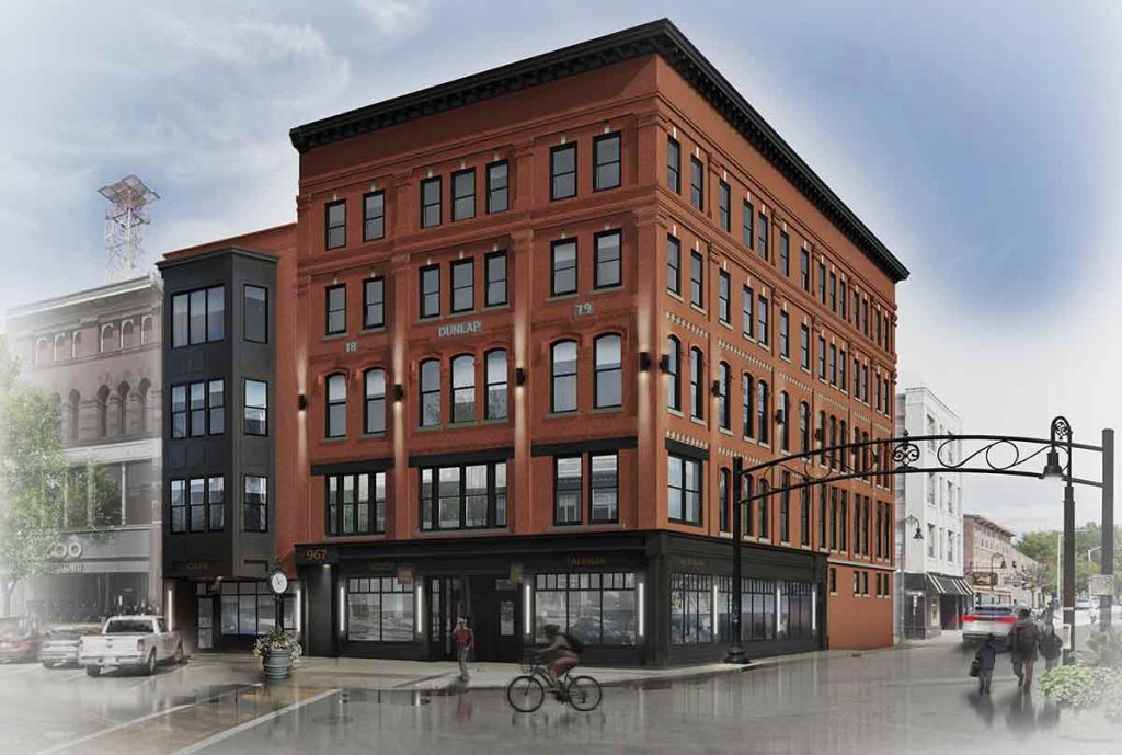 A four-story red-brick building with large windows on a city street corner, featuring ground-floor shops, pedestrians, and a cyclist under a cloudy sky.