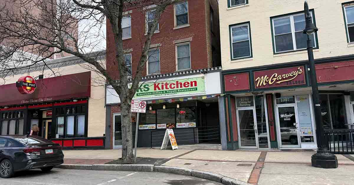 A street view showing three businesses: The Pub, KS Kitchen, and McGarvey’s. A tree, streetlamp, and parked car are visible on the sidewalk in front of the shops.