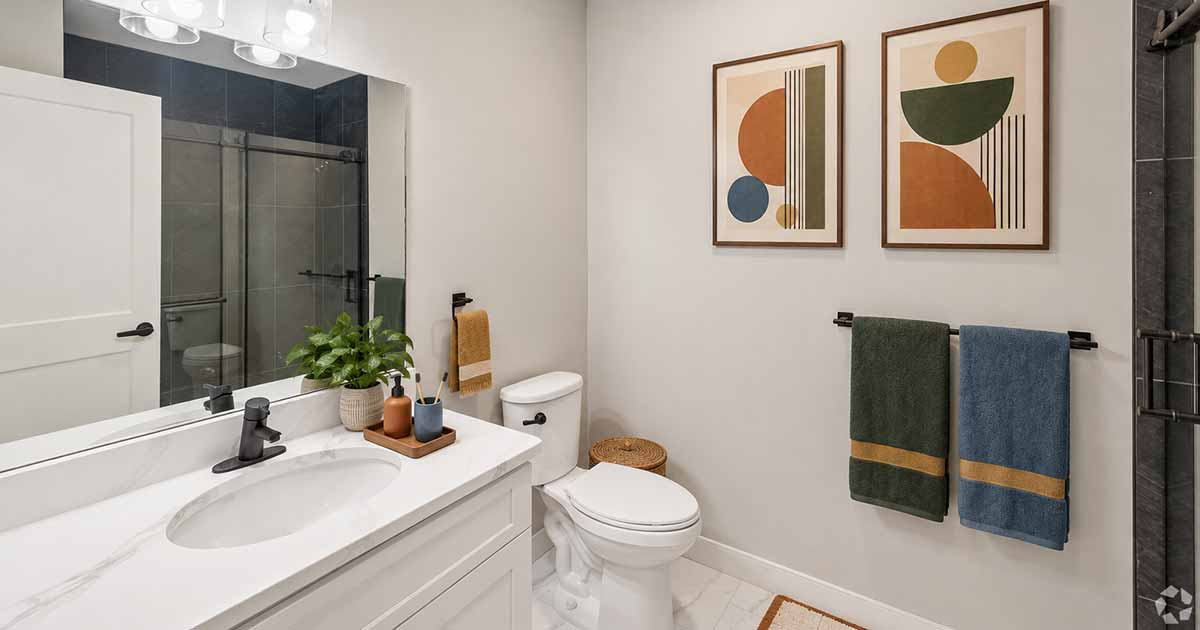 A bathroom featuring a white vanity with a marble countertop, a toilet, and two abstract art prints on the wall.