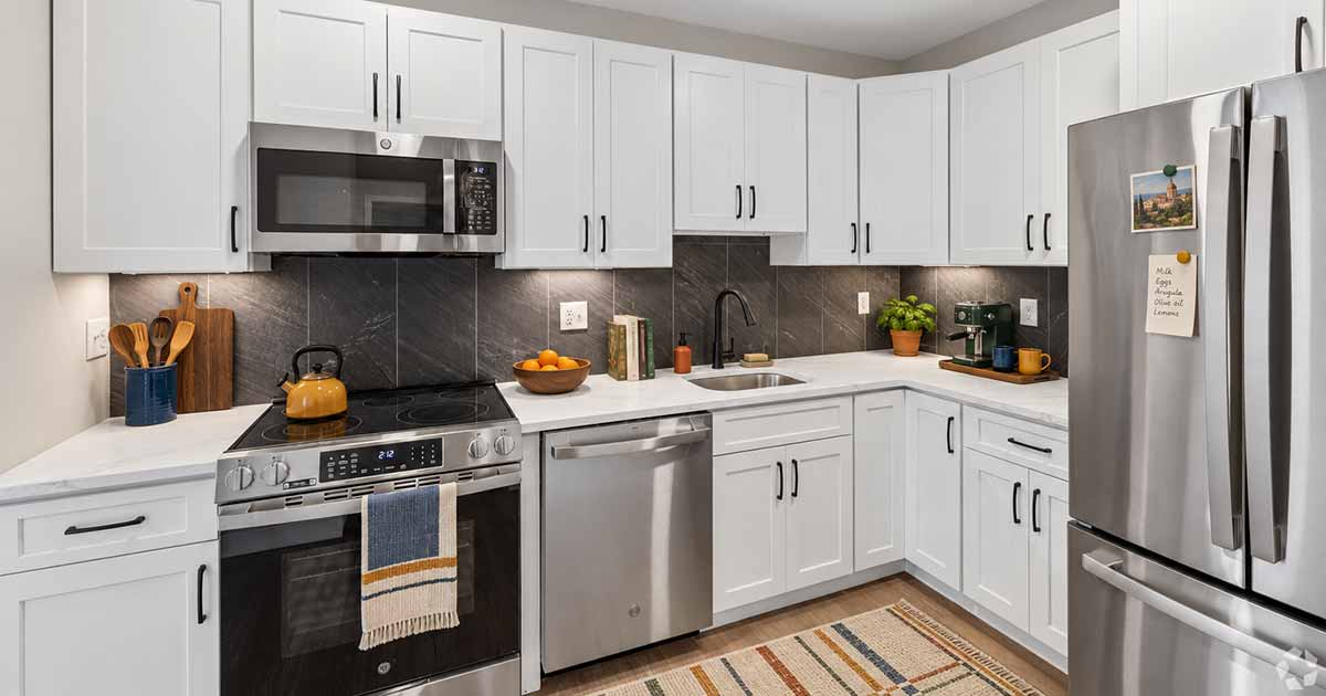 A kitchen with white cabinets, stainless steel appliances, and a dark tile backsplash.