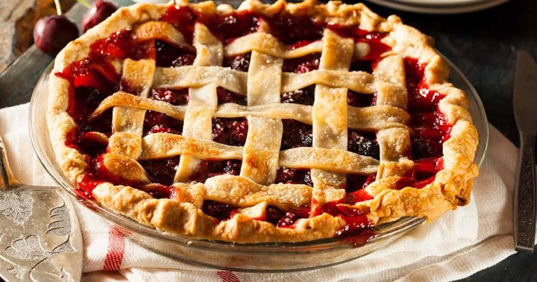 A cherry lattice-crust pie in a glass dish on a cloth napkin.